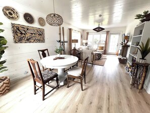 Een eetgedeelte met een ronde tafel en stoelen, omringd door wanden met kunstwerken en een plafond met hangende lampen.