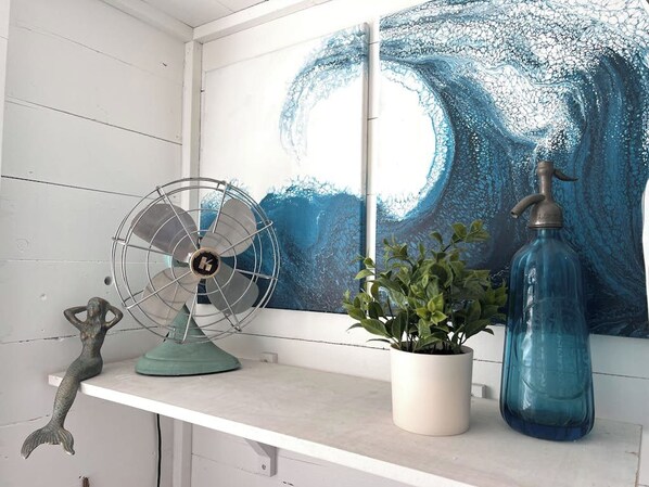 A room with a white shelf holding a fan, a potted plant, and a blue bottle. - Stunning 1BR Oceanview -Patio -Washer Dryer- Hottub-Firepit (Moclips)