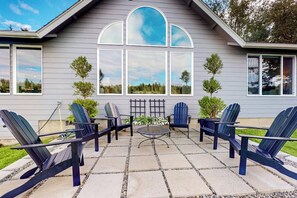 A patio with Adirondack chairs and a table, a large window with a view, and a small tree. - 7BR Property with water views & private beach (Shelton)