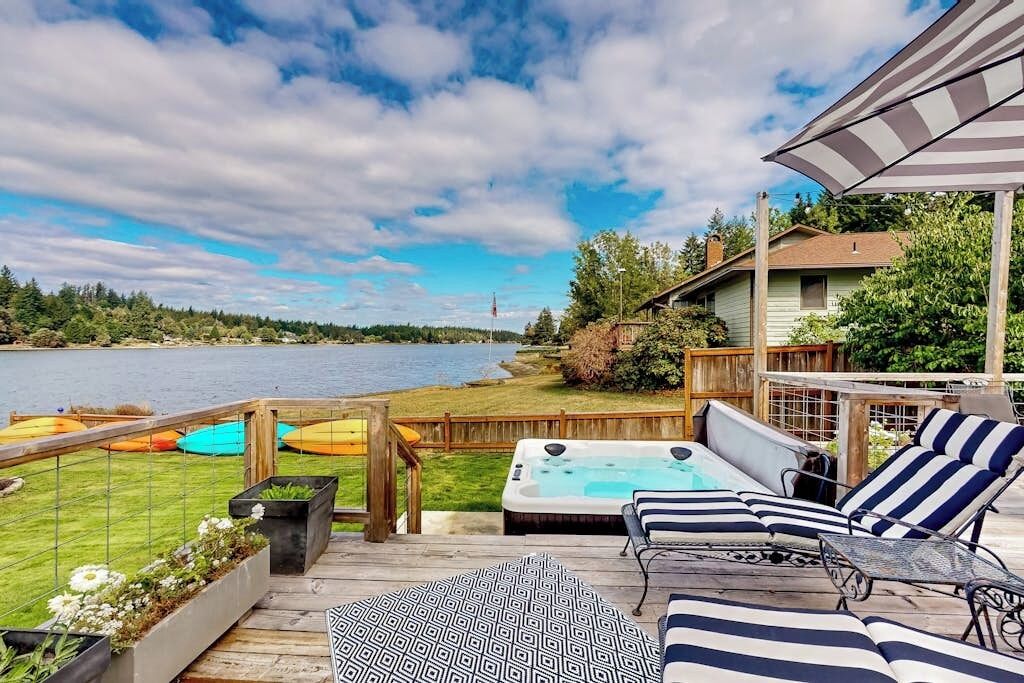 A deck with a hot tub, lounge chairs, and a view of a lake.