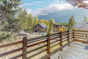 Eine Holzterrasse mit Blick auf eine gebirgige Landschaft, mit einigen Gebäuden, darunter eine Hütte und ein modernes Haus.