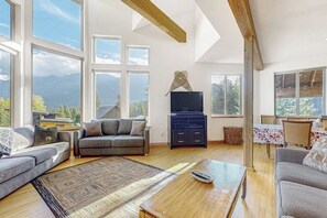 Ein geräumiges Wohnzimmer mit großem Fenster, einem Flachbildfernseher und einem Holztisch.