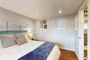 Een slaapkamer met een bed, een nachtkastje, een wandplank met een vaas en een schilderij.