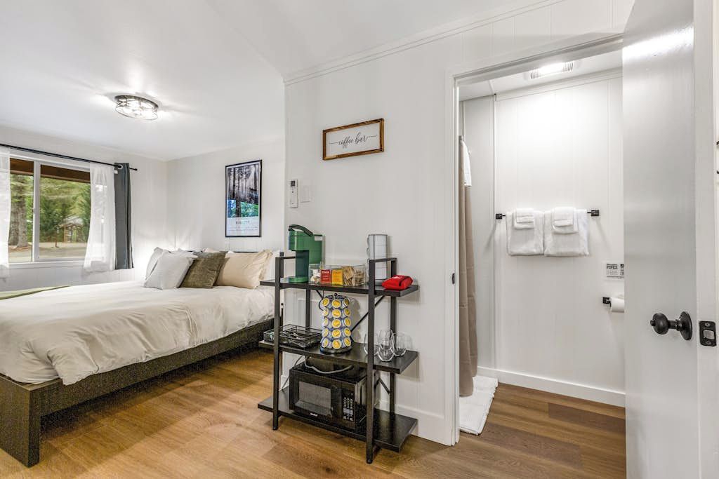 Un dormitorio con una cama, una estantería con objetos diversos, una ventana y una puerta.