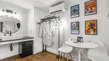 A modern bathroom with a large mirror, white sink, and a black refrigerator. There are two white chairs and a small table with a sign.
