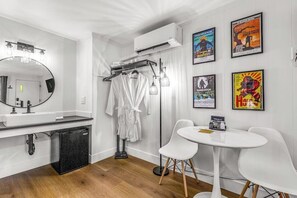 Un baño moderno con un espejo grande, un lavamanos blanco y un refrigerador negro. Hay dos sillas blancas y una mesita con un letrero.