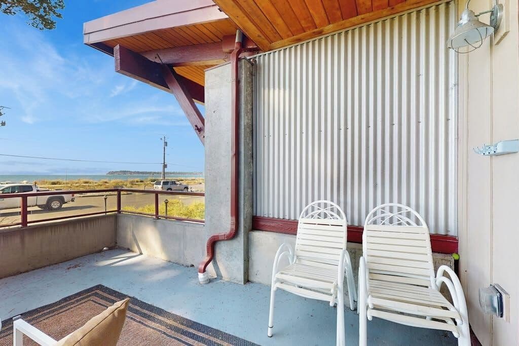 A balcony with two white chairs, a concrete floor, and a view of the road.