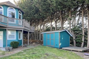 Une maison à deux étages avec un balcon, un petit abri de jardin et une cour entourée d’arbres.
