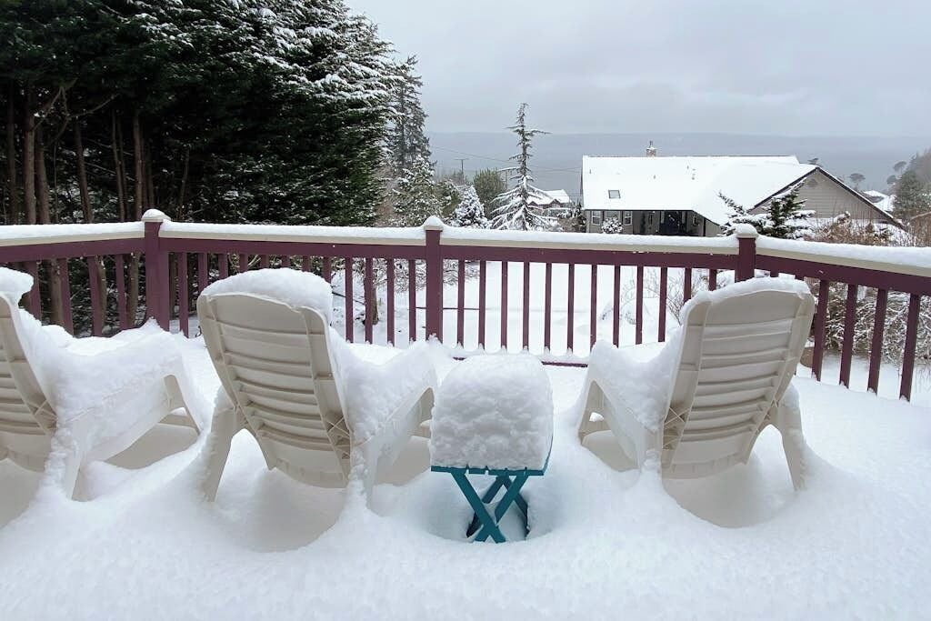A snow-covered deck with outdoor seating and a view of a house in the background.