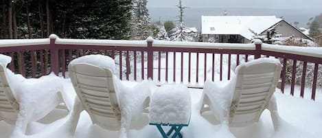 A snow-covered deck with outdoor seating and a view of a house in the background.