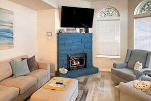 A living room with a fireplace, a flat-screen TV mounted above it, and two sofas. - Large 3BR Bayview Dog Friendly - Fireplace (Camano Island)