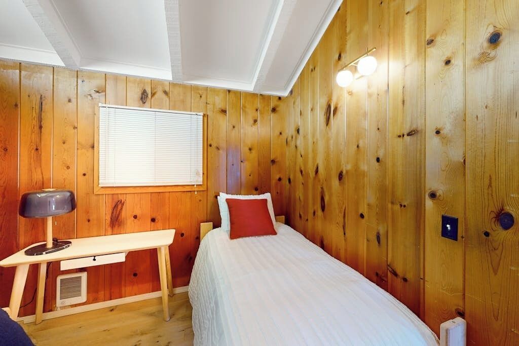 A wooden-paneled room with a bed, a desk, and a window.