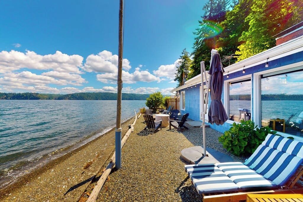 A lakeside property with a patio, lounge chairs, and a table with chairs.
