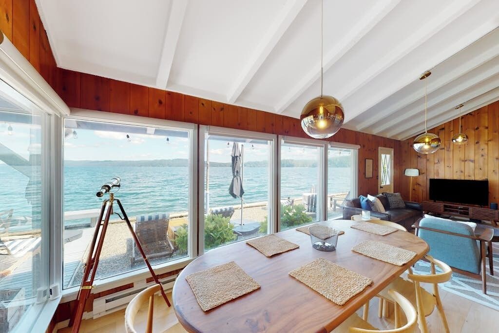 Amplia habitación con una gran mesa de madera, varias ventanas que ofrecen vistas al mar y una zona de estar acogedora con televisión.
