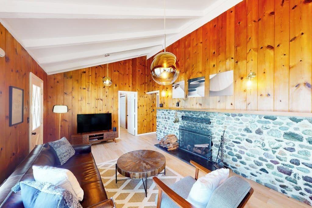 Ein gemütliches Wohnzimmer mit Kamin aus Stein, Holzwänden, einer Ledersofa und einem Fernseher.