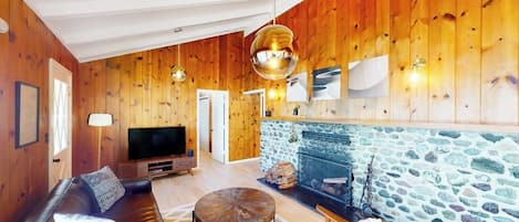 Ein gemütliches Wohnzimmer mit Kamin aus Stein, Holzwänden, einer Ledersofa und einem Fernseher.