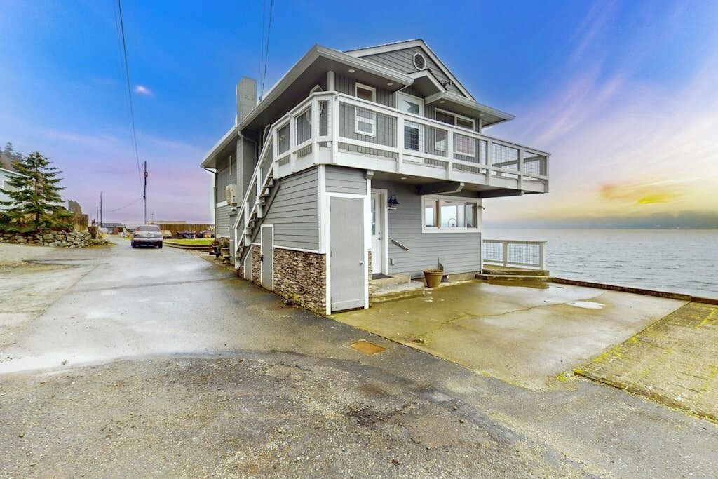 A two-story waterfront house with a balcony, a staircase leading to the upper floor, and a view of the water.