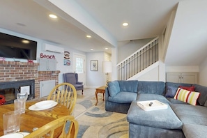 A living room with a fireplace, a sofa, a dining table with chairs, and a staircase. - 3 BR waterfront home with stunning views (Camano Island)