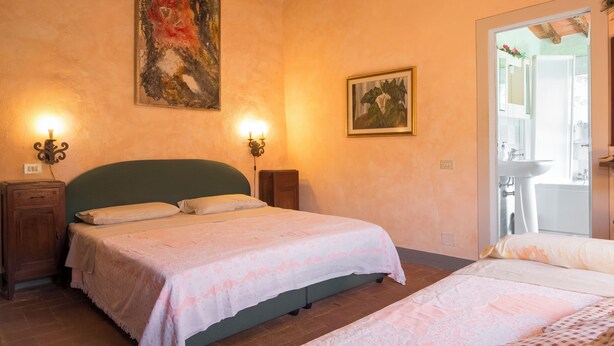 Quarto com cama, duas mesas de cabeceira, um quadro pendurado na parede e uma porta para o banheiro.