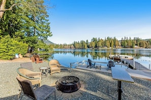 A lakeside patio with outdoor furniture, a fire pit, and a dock extending into the water. - Lakefront views with hot tub, firepit, & deck (Sedro-Woolley)