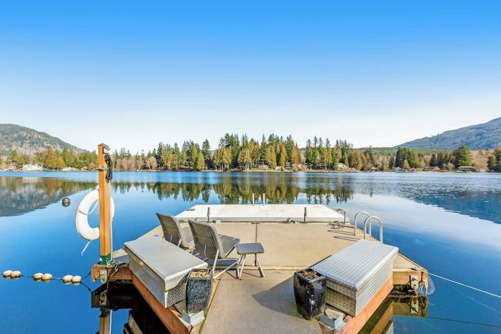 A boat docked at a calm lake with a clear view of the surrounding forest and hills.
