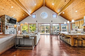 A spacious interior with a high ceiling, a stone fireplace, a kitchen area, and a seating area with a view. - Lakefront views with hot tub, firepit, & deck (Sedro-Woolley)