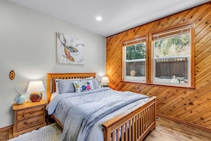 A bedroom with a wooden headboard, a bed with a blue blanket, two bedside lamps, a small vase, and a painting on the wall. - Lakefront views with hot tub, firepit, & deck (Sedro-Woolley)