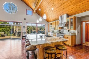 A spacious kitchen with a large island, wooden cabinets, and a view through the glass doors. - Lakefront views with hot tub, firepit, & deck (Sedro-Woolley)