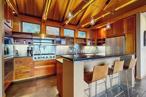 A modern kitchen with wooden cabinets, a central island with bar stools, and pendant lighting.