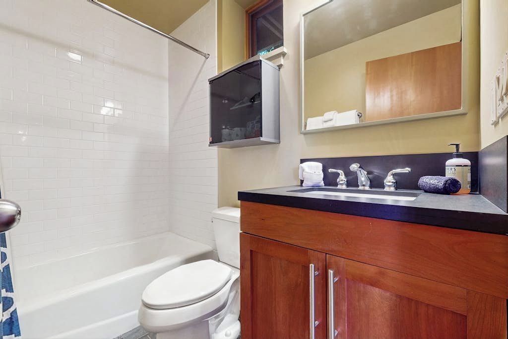 A bathroom with a white toilet, a bathtub, a wooden vanity with a sink, and a mirror above the vanity.