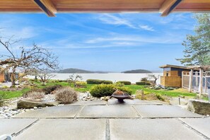A patio with a view of a lake and mountains, a fire pit, and a wooden structure.