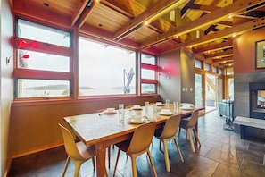 A dining area with a wooden table set for four, large windows, and a fireplace.