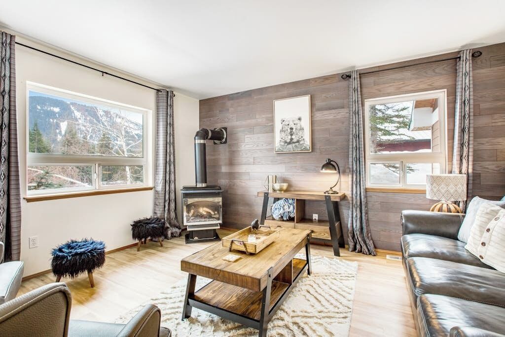 Ein gemütliches Wohnzimmer mit Kamin, Couch und Blick ins Freie, dazu ein Holztisch.