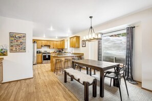 A spacious kitchen with wooden cabinets, a central island, and a dining area with a bench and chairs. - ski-in and out 3BR with mountain views & fireplace (Snoqualmie Pass)