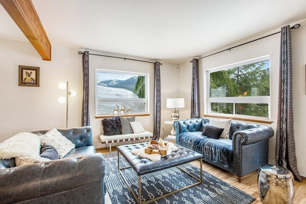 A modern living room with a sofa, a coffee table, and a view of mountains through large windows.