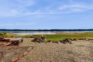 A pebbled beach area with a bench and a wooden structure, overlooking a calm body of water and distant hills. - 2BR Waterfront Home with Private Beach Access (Belfair)
