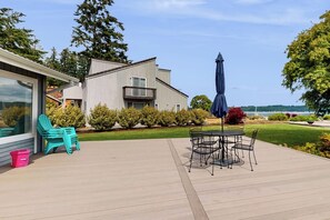 A deck with outdoor furniture, a view of a house, and a body of water in the background. - 2BR Waterfront Home with Private Beach Access (Belfair)