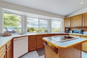 A modern kitchen with a large island, wooden cabinets, and a view of the outdoors. - 2BR Waterfront Home with Private Beach Access (Belfair)