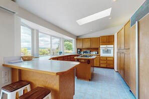 A modern kitchen with a large island, wooden cabinets, and a view through the windows. - 2BR Waterfront Home with Private Beach Access (Belfair)