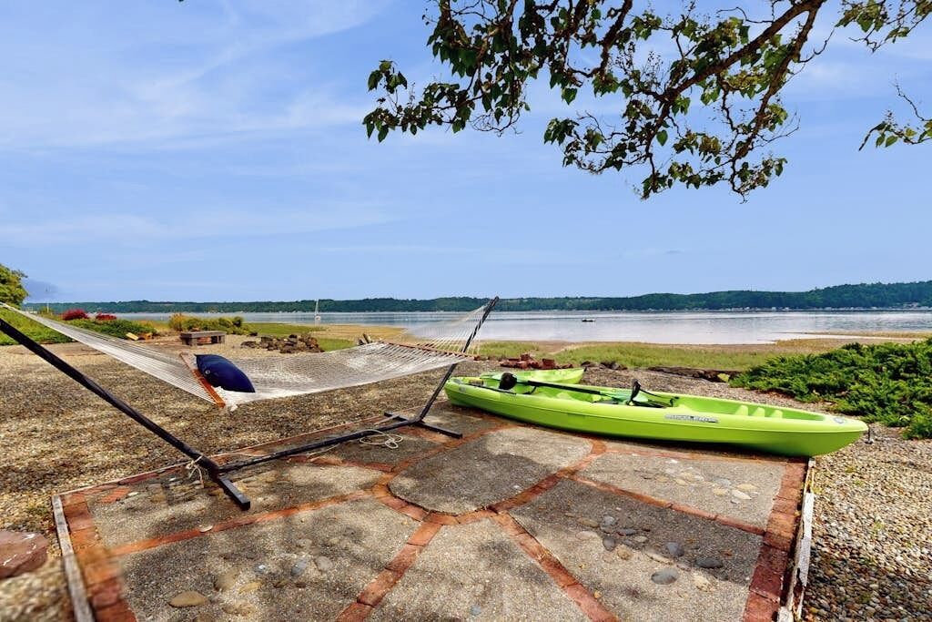 Una hamaca y un kayak verde sobre una terraza de piedra con vista al agua.