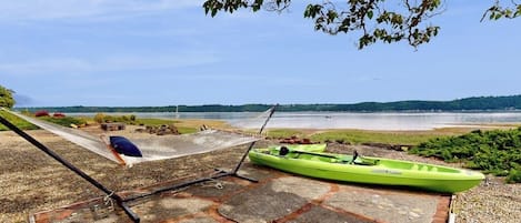 A hammock and a green kayak on a stone deck overlooking a body of water.