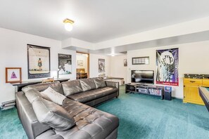 A living room with a leather sofa, a flat-screen TV, and various posters on the walls. - 3BR Waterview - Fireplace - Balcony (Hansville)