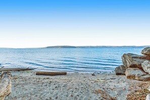 A beach with clear blue water, a sandy shore, and large rocks. - 3BR Waterview - Fireplace - Balcony (Hansville)
