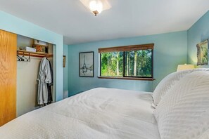 A bedroom with a bed, a window with a view of trees, a coat rack, and a painting on the wall. - 3BR Waterview - Fireplace - Balcony (Hansville)