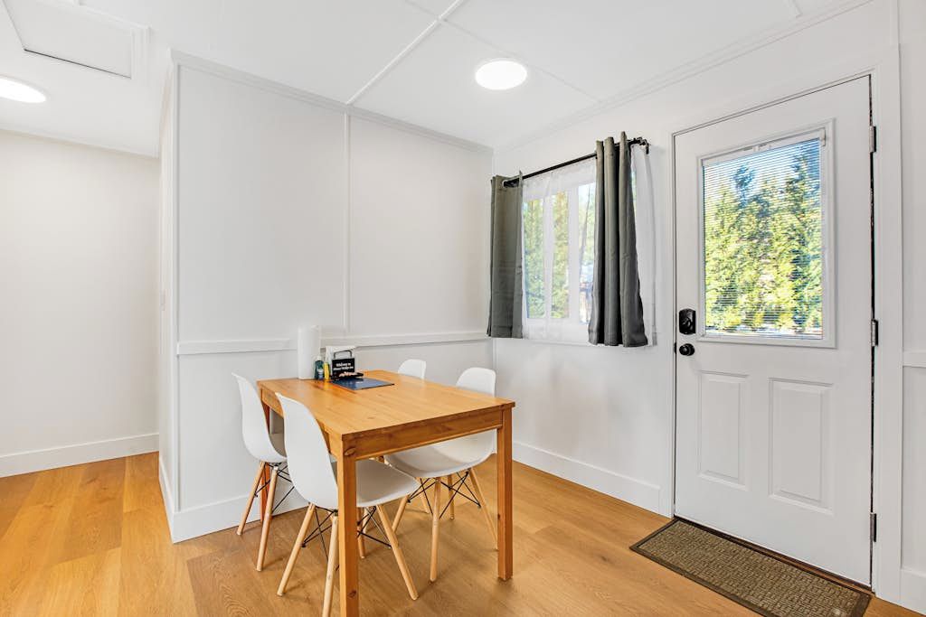 Ein Zimmer mit einem Holztisch, weißen Stühlen, einer weißen Tür und einem Fenster mit Vorhängen.