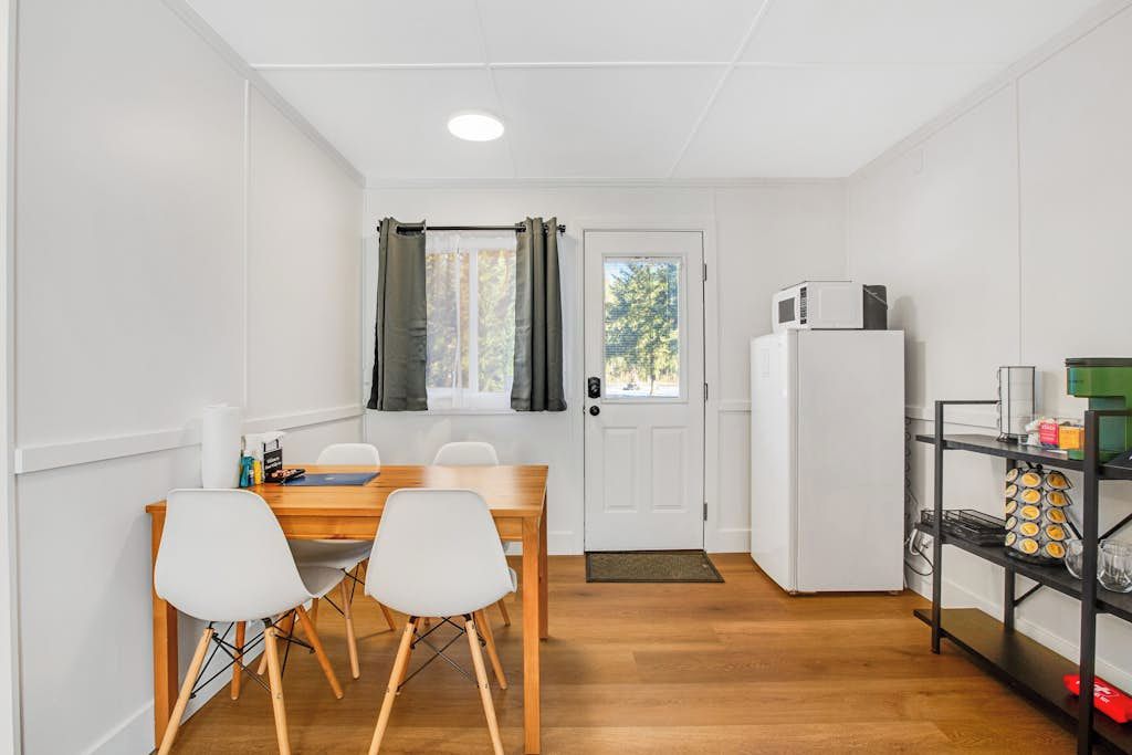 Cocina compacta con mesa, sillas, refrigerador y ventana con cortinas.