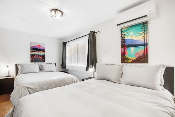 Una habitación de hotel con dos camas, un ventanal con cortinas y dos cuadros en las paredes.
