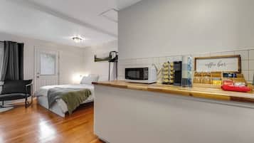 Een kleine kamer met een kitchenette, een bed en een stoel.