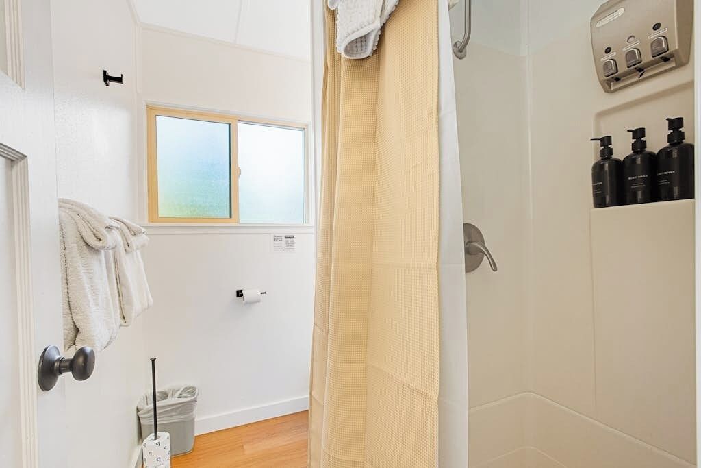 A bathroom with a shower curtain, a window, a towel rack, a toilet paper holder, and a shelf with toiletries.