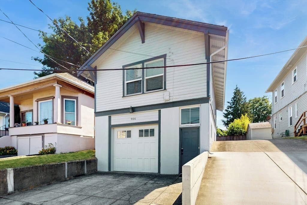 A two-story residential building with a garage, a front porch, and a small front yard.